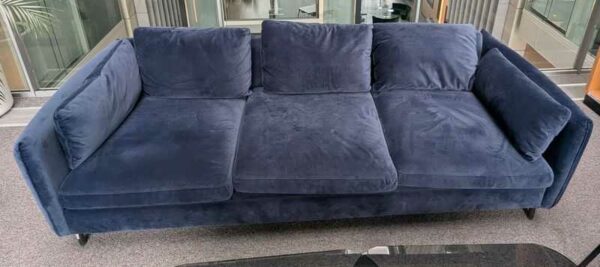 Canapé 3/4 places de marque MADE.COM recouvert de velours bleu, coussins amovibles, pieds en acier laqué noir. 60 x 220 x 95 cm. Localisation : 2 ème coursive