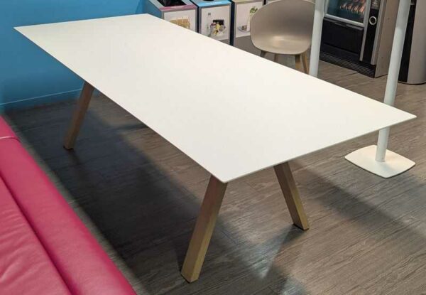 Table rectangulaire, plateau en bois stratifié blanc reposant sur 4 pieds obliques en bois naturel. 73 x 240 x 100 cm. Localisation : 4 est
