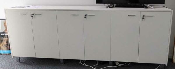 Armoire basse ou enfilade en bois laqué blanc, ouvrant par 6 portes, piètement et poignées en acier chromé. 100 x 262 x 45 cm. Localisation : 7 ouest