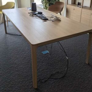 Table de réunion en bois couleur chêne clair, plateau rectangulaire à bords arrondis avec 2 trappes passe-câbles. 76 x 240 x 120 cm. Localisation : 6 ouest