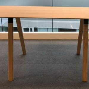 Table haute en bois couleur chêne clair plateau rectangulaire reposant sur 4 pieds obliques. 104 x 200 x 90 cm. Localisation : 6 passerelle