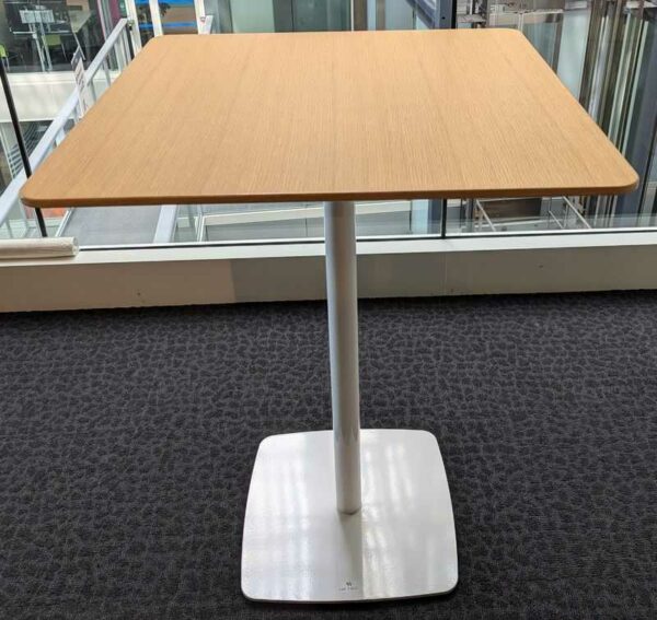 Table haute ou mange debout à plateau carré couleur chêne clair reposant sur un pied colonne en acier laqué blanc. Localisation : 5 ouest