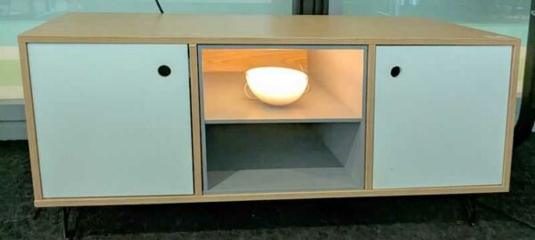 Meuble bas en bois couleur chêne clair avec une niche et 2 portes en bois laqué blanc ouvrant sur 1 étagère, piètement en épingle en acier laqué noir. 50 x 110 x 40 cm. Localisation : 5 ouest