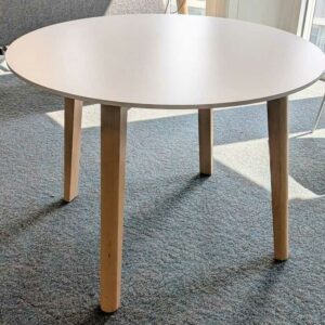 Table ronde en bois, plateau blanc reposant sur 4 pieds en bois naturel. 73 x 100 cm. Localisation : 5 est