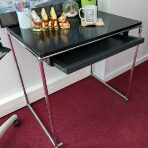 Table de marque USM HALLER, plateau en bois de couleur noire avec une tablette rétractable en ceinture, reposant sur une structure en acier chromé. 70 x 76 x 54 cm. Localisation : Canada 1er (2B01) – Image 2