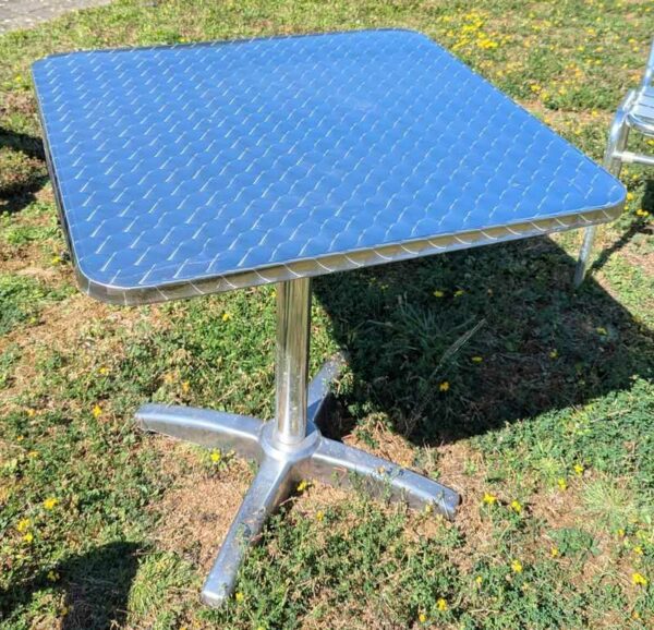 Table carrée de marque RODET en aluminium, plateau en bois stratifié revêtu d'inox. 73 x 70 x 70 cm. 6 unités. Vendu avec faculté de réunion. Localisation : extérieur