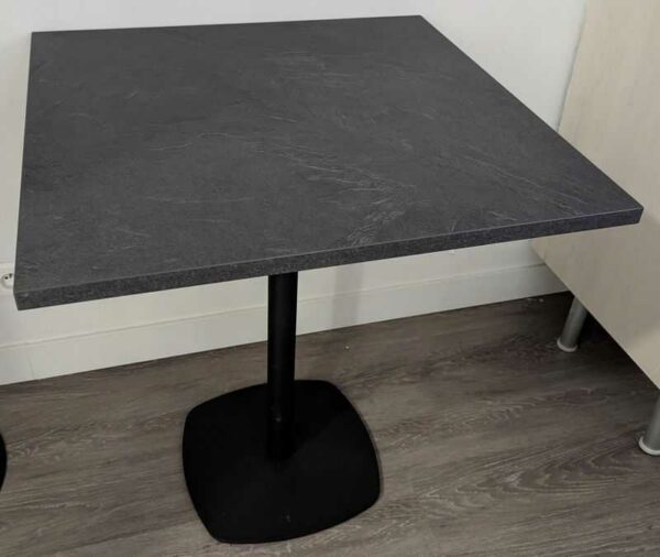 Table carrée à plateau en bois stratifié effet ardoise reposant sur un piètement colonne en acier laqué noir. 77 x 70 x 70 cm. 4 unités. Vendu avec faculté de réunion. Localisation : Theta rdc, 1er (0t33, cafet)