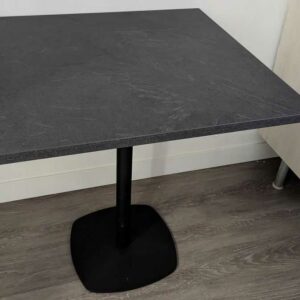 Table carrée à plateau en bois stratifié effet ardoise reposant sur un piètement colonne en acier laqué noir. 77 x 70 x 70 cm. 4 unités. Vendu avec faculté de réunion. Localisation : Theta 1er cafet