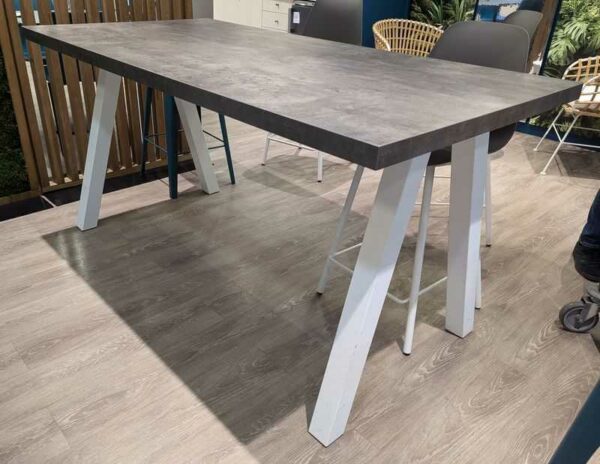 Table haute plateau rectangulaire en bois effet béton, piètement oblique en acier laqué blanc. 90 x 180 x 90 cm. Localisation : Theta 1er cafet