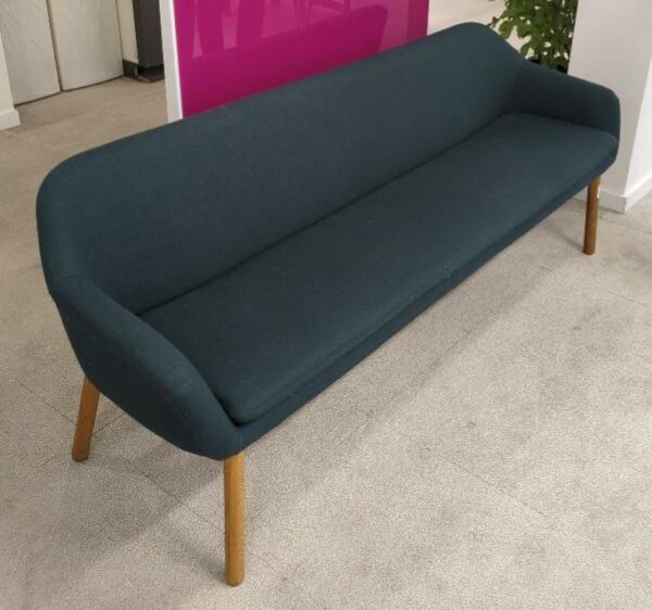 Canapé de marque Bolia recouvert de feutrine vert bouteille, coussin d'assise amovible, piètement en bois naturel. 77 x 202 x 57 cm. Localisation : 9 avenue Percier 75008 Paris