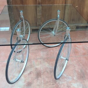 Table montée sur 4 roues de vélo, plateau carré en verre transparent (2 éclats à 2 coins). 74 x 120 x 120 cm. Localisation : 8 rue de la Fossé aux Leux 91700 Ste Geneviève des Bois