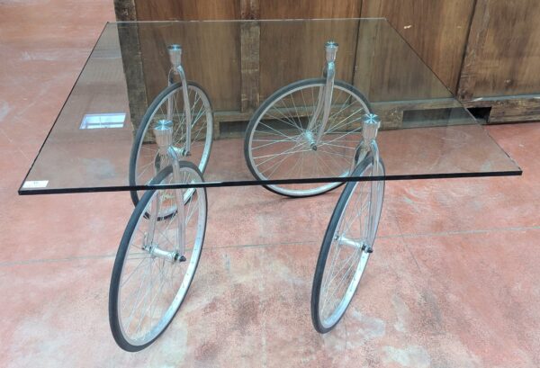 Table montée sur 4 roues de vélo, plateau carré en verre transparent (2 éclats à 2 coins). 74 x 120 x 120 cm. Localisation : 8 rue de la Fossé aux Leux 91700 Ste Geneviève des Bois