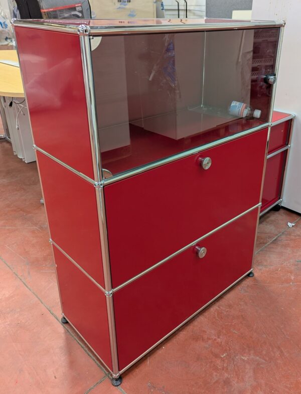Meuble de marque USM HALLER de couleur rouge à 3 compartiments dont 1 ouvrant par 1 porte vitrée (fermée à clé) et 2 par portes à abattant. 109 x 77 x 38 cm. Localisation : 8 rue de la Fossé aux Leux 91700 Ste Geneviève des Bois