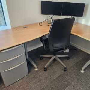 Bureau d'angle en bois couleur miel clair reposant sur un piètement métallique triple en acier gris. Dimensions: 160 x 160 cm. On y joint son caisson à hauteur d'appui. Quantités disponibles: 830 unités. Localisation : 8 av. de Lunca - 78180 Montigny-le-Bretonneux. – Image 4