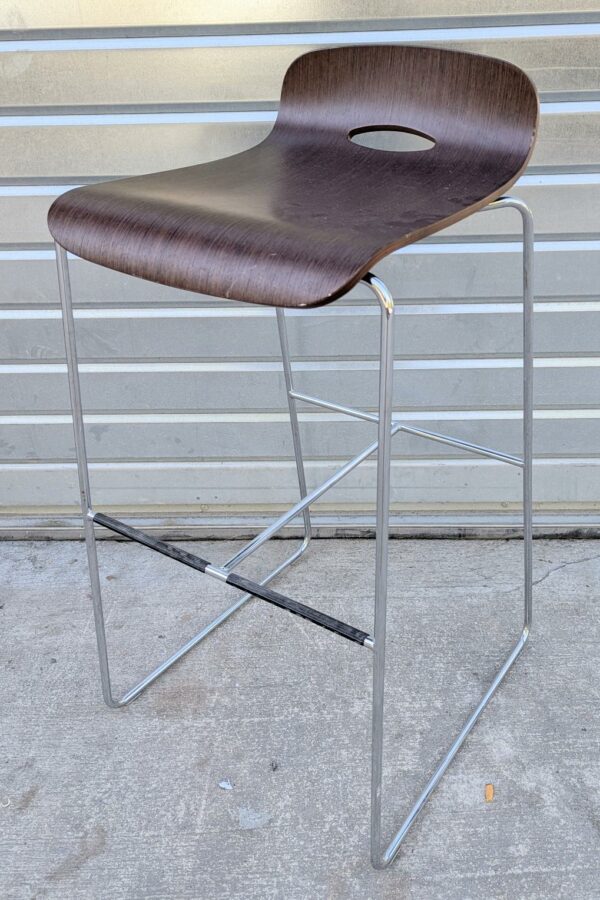Tabouret haut coque en bois contreplaqué reposant sur une structure en acier chromé, piètement luge avec entretoise et repose pied. 88 x 42 x 52 cm. 7 unités. Vendu à l'unité avec faculté de réunion. Localisation: 10 rue du Ballon - 93160 Noisy-Le-Grand.
