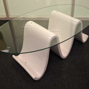 Table basse en  forme de vague, support en bois laqué blanc, plateau ovale en verre transparent. 42 x 120 x 70 cm. 1 unité. Localisation: Entresol salle café codir
