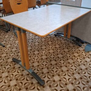 Table 4 personnes, plateau rectangulaire en bois stratifié moucheté bleu, piétement en bois et métal. 74 x 120 x 80 cm. 16 unités. Localisation: Rie