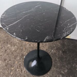 Table basse dans le goût de Gueridon Verde Alpi édition Knoll, plateau en marbre de couleur noir reposant sur un pied tulipe en métal de couleur noir sur base circulaire. (accident) Dim : 50 x 42 cm. Localisation : 30 rue Beauregard - 60440 Nanteuil-le-Haudouin