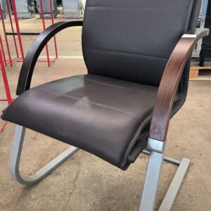 Fauteuil recouvert de cuir marron, accoudoirs en bois de couleur chêne, piétement porte-à-faux en métal de couleur gris clair. Dim : 94 x 62 x 60 cm. Localisation : 34 avenue du Général Patton 02880 Crouy