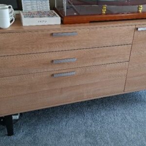 Buffet bas en bois couleur chêne ouvrant par 1 tiroir coulissant, 1 porte (à droite ou gauche) sur un espace pouvant contenir un mini réfrigérateur, et 2 portes à abattant, piétement en acier laqué noir. 90 x 180 x 50 cm. 3 unités. Vendu à l'unité avec faculté de réunion. Localisation: 48 rue Cambon - 75001 Paris