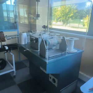 Machine à bobiner et enrouler les fils pour ligament artificiel, à 2 postes de travail, avec dispositifs de guidage et de tension, bobines et carter de protection transparent. Montée sur bâti avec commande intégrée.